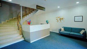 A reception desk with a sign, a globe, flags, a world map, a staircase, and a blue sofa. - Kichik Gala 98 (Baku)