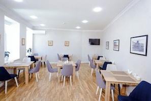 A conference room with multiple tables and chairs, a flat-screen TV, framed pictures on the walls, and a wooden floor. - Kichik Gala 98 (Baku)
