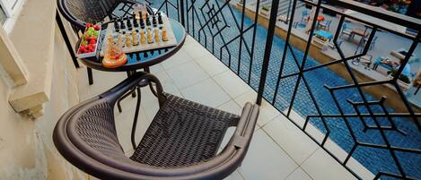 A balcony with a table set for dining, a chair, and a view of a courtyard with shops and outdoor seating.
