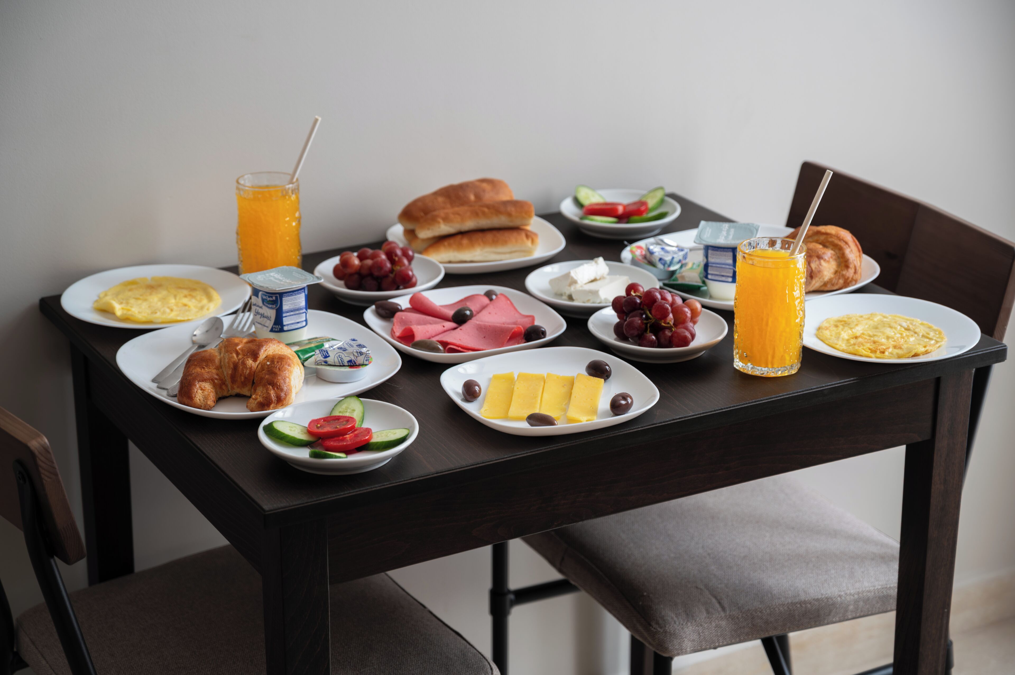 A breakfast table with plates of food, a glass of orange juice, and a croissant.