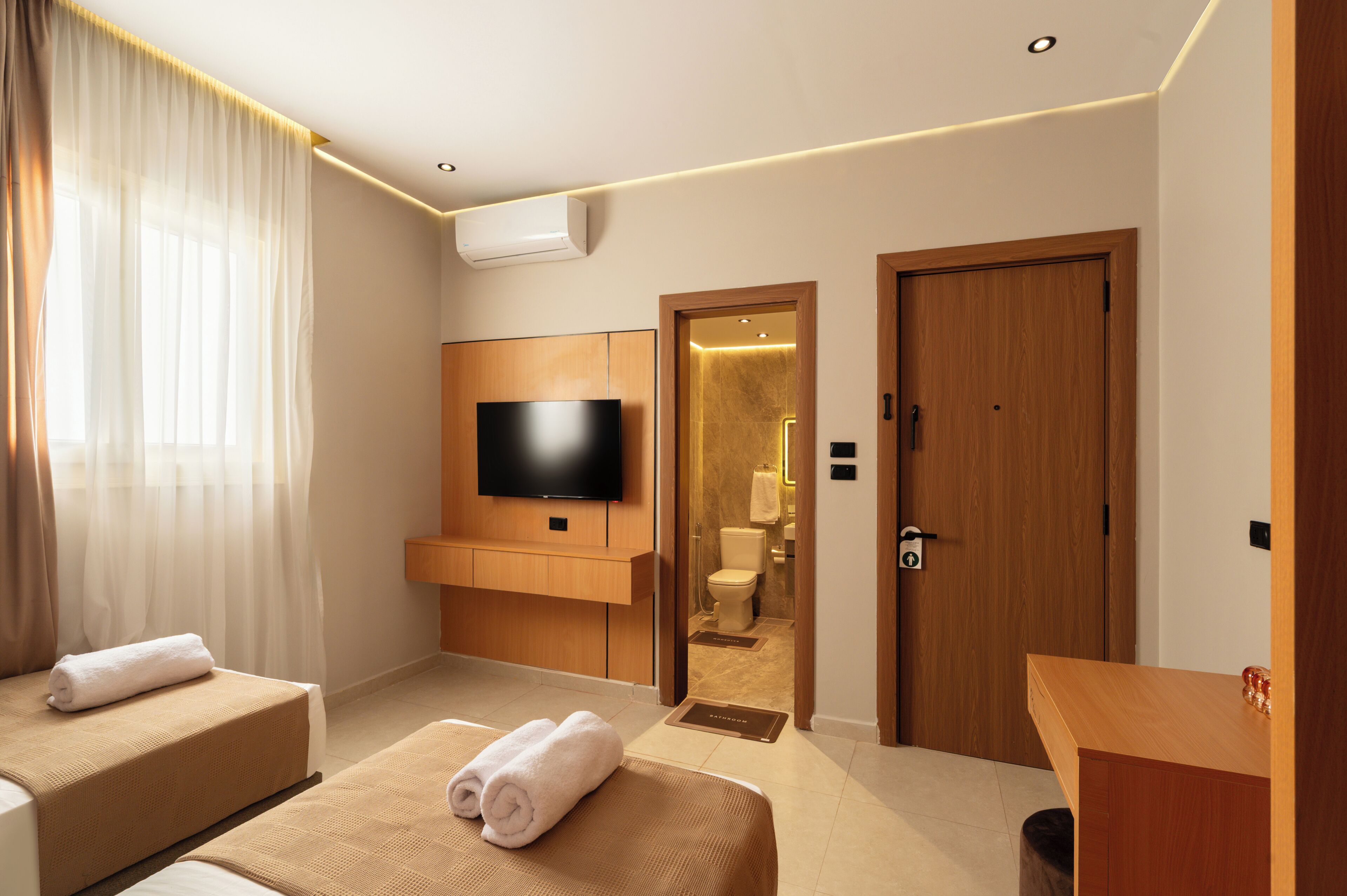 A hotel room with a bed, a TV, a wooden wardrobe, a bathroom, and a door.