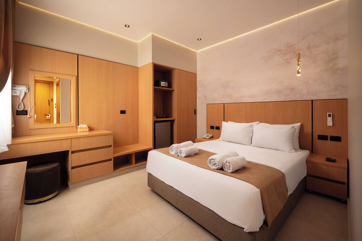 A modern hotel room with a bed, bedside tables, a desk, a mirror, and a wardrobe.