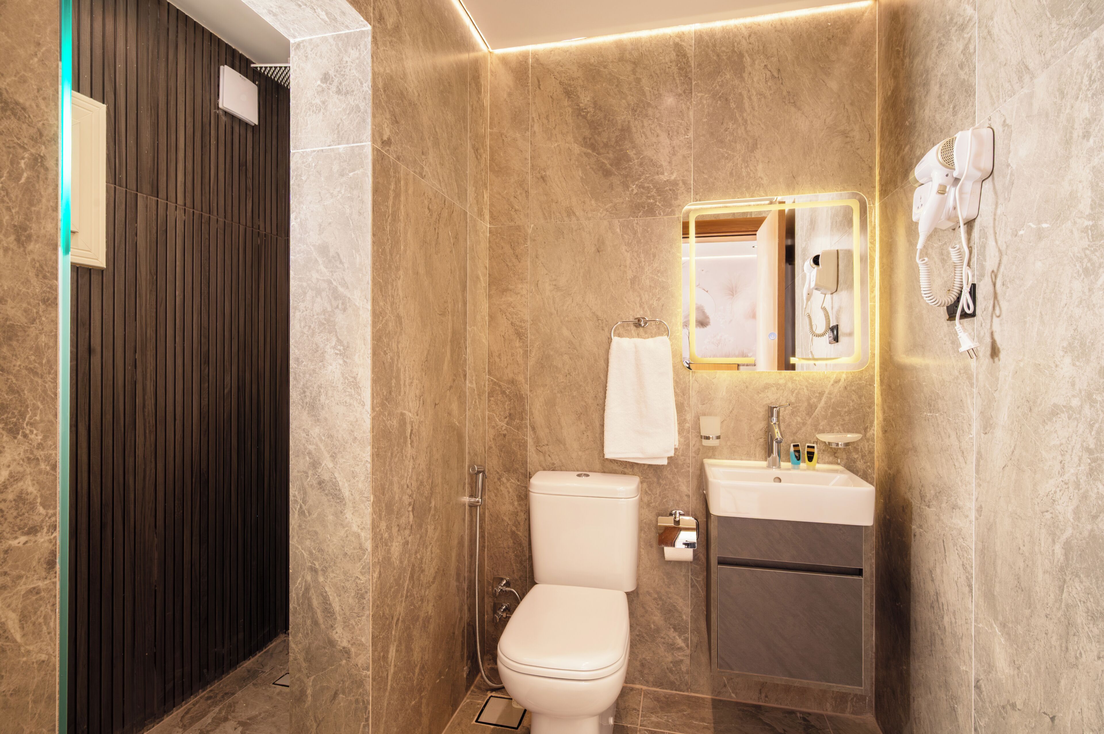 A modern bathroom with a toilet, sink, and hairdryer mounted on the wall.