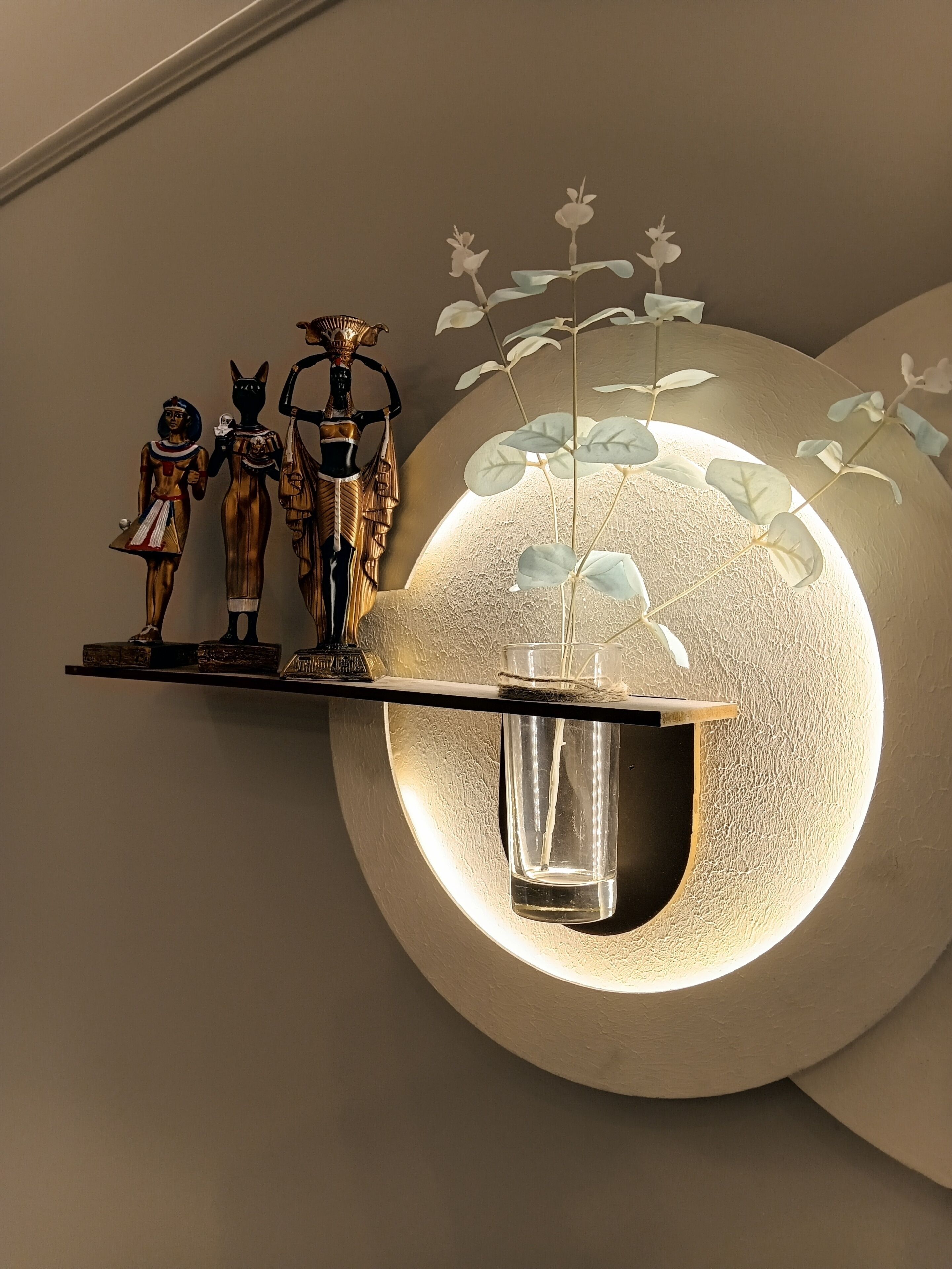 A wall-mounted shelf with decorative figures and a vase with a plant.