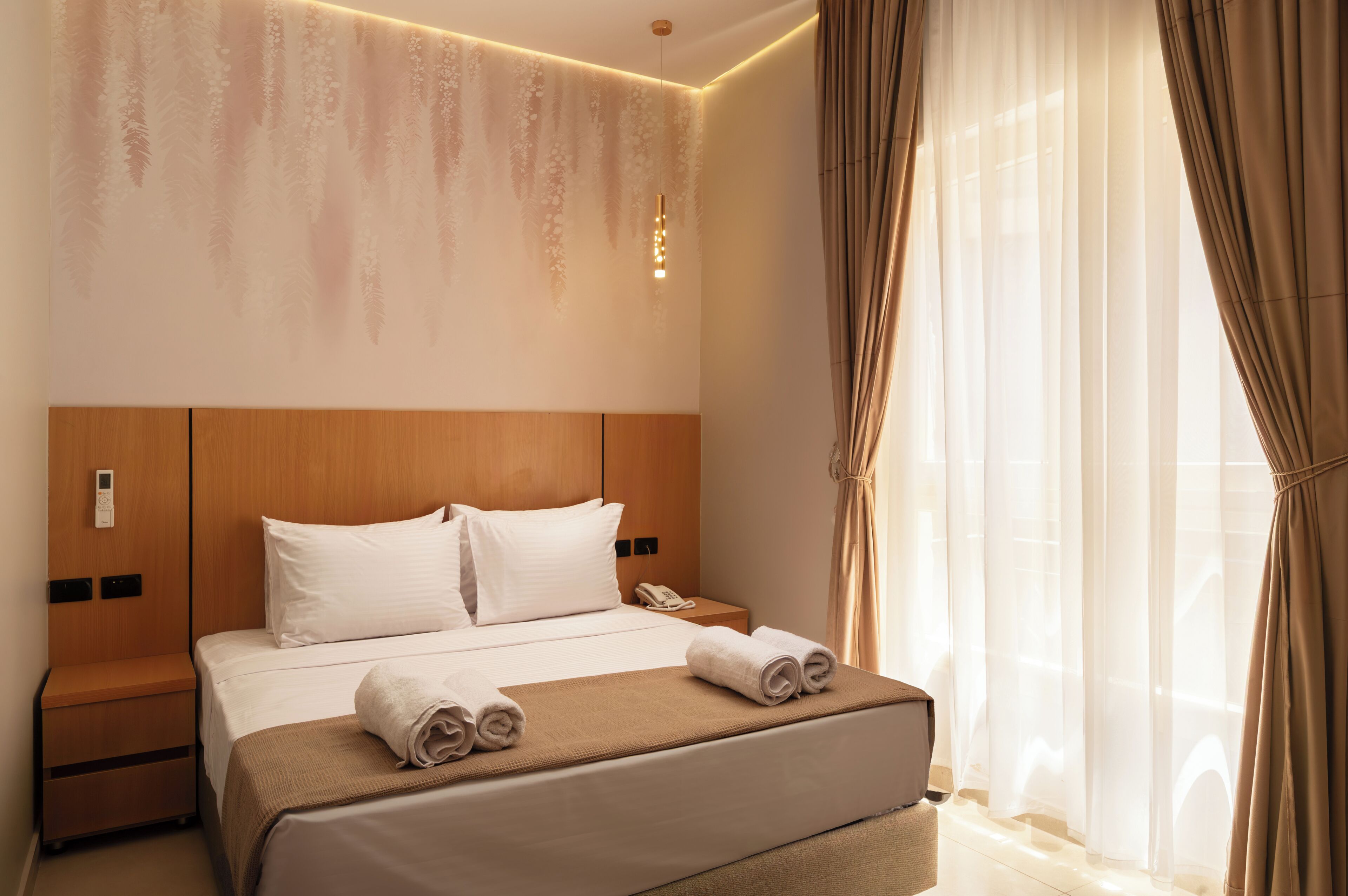 Une chambre d’hôtel avec un lit, des tables de chevet, une lampe fixée au mur et une fenêtre avec des rideaux.
