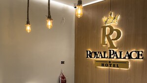 Ein Empfangsschalter mit Marmorplatte, eine Holzwand mit einem Schild ‚Royal Palace Hotel‘ und drei Pendelleuchten.