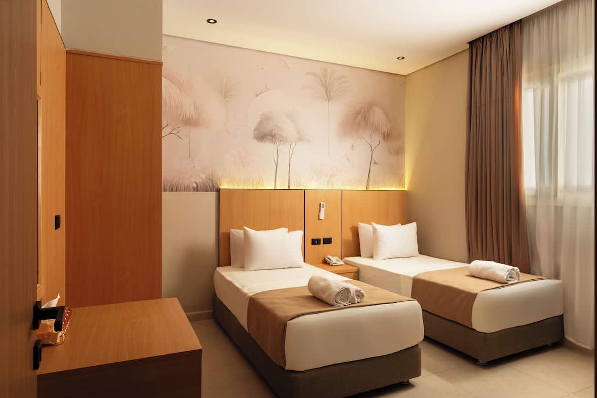 A hotel room with two beds, a wooden wardrobe, a desk, and a wall mural.