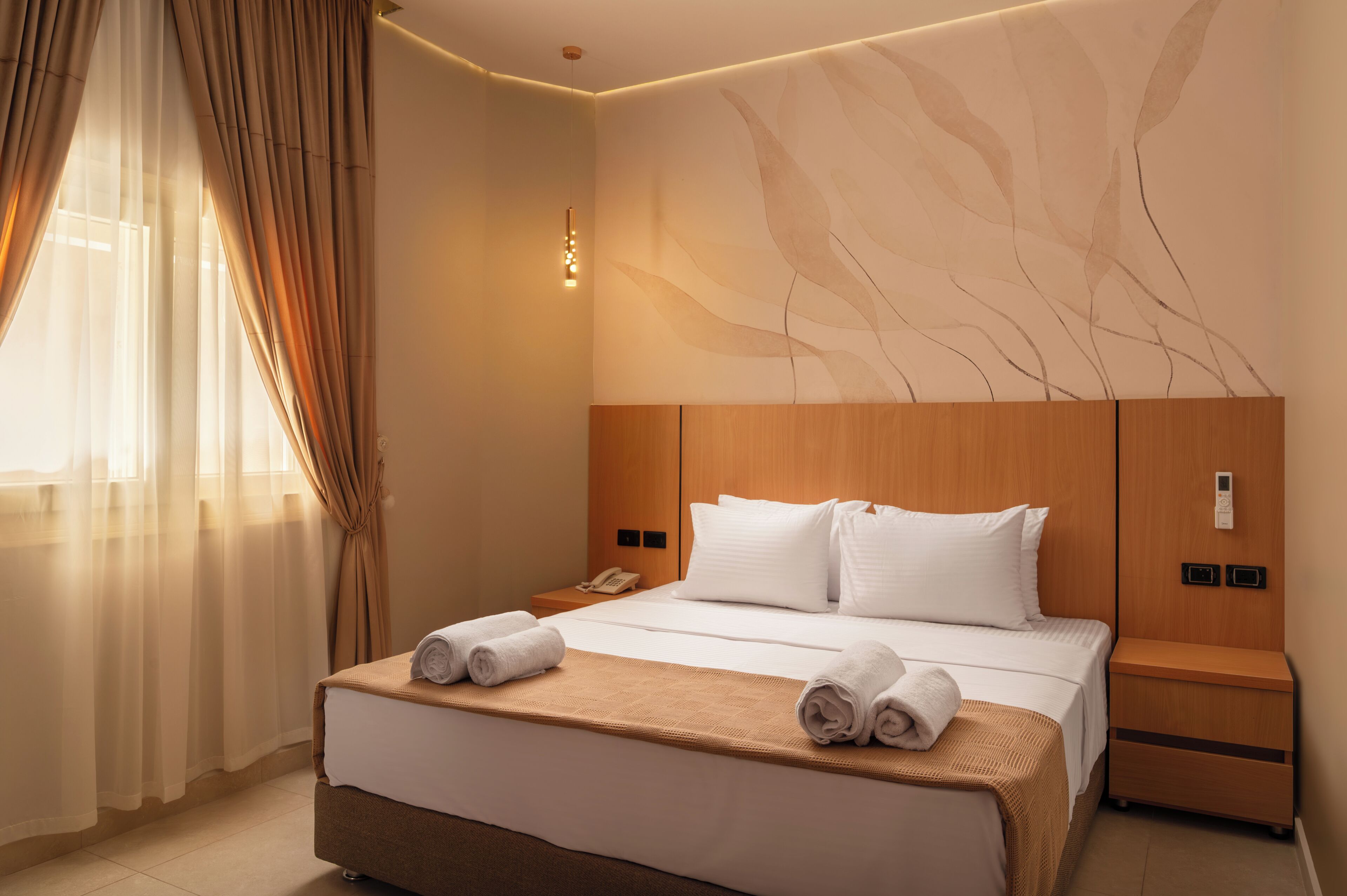 A hotel room with a bed, bedside tables, a nightstand, a wall-mounted phone, and a window with curtains.
