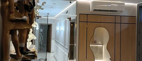 A modern hotel corridor with a wooden cabinet, a wall-mounted air conditioner, and a statue on a pedestal.