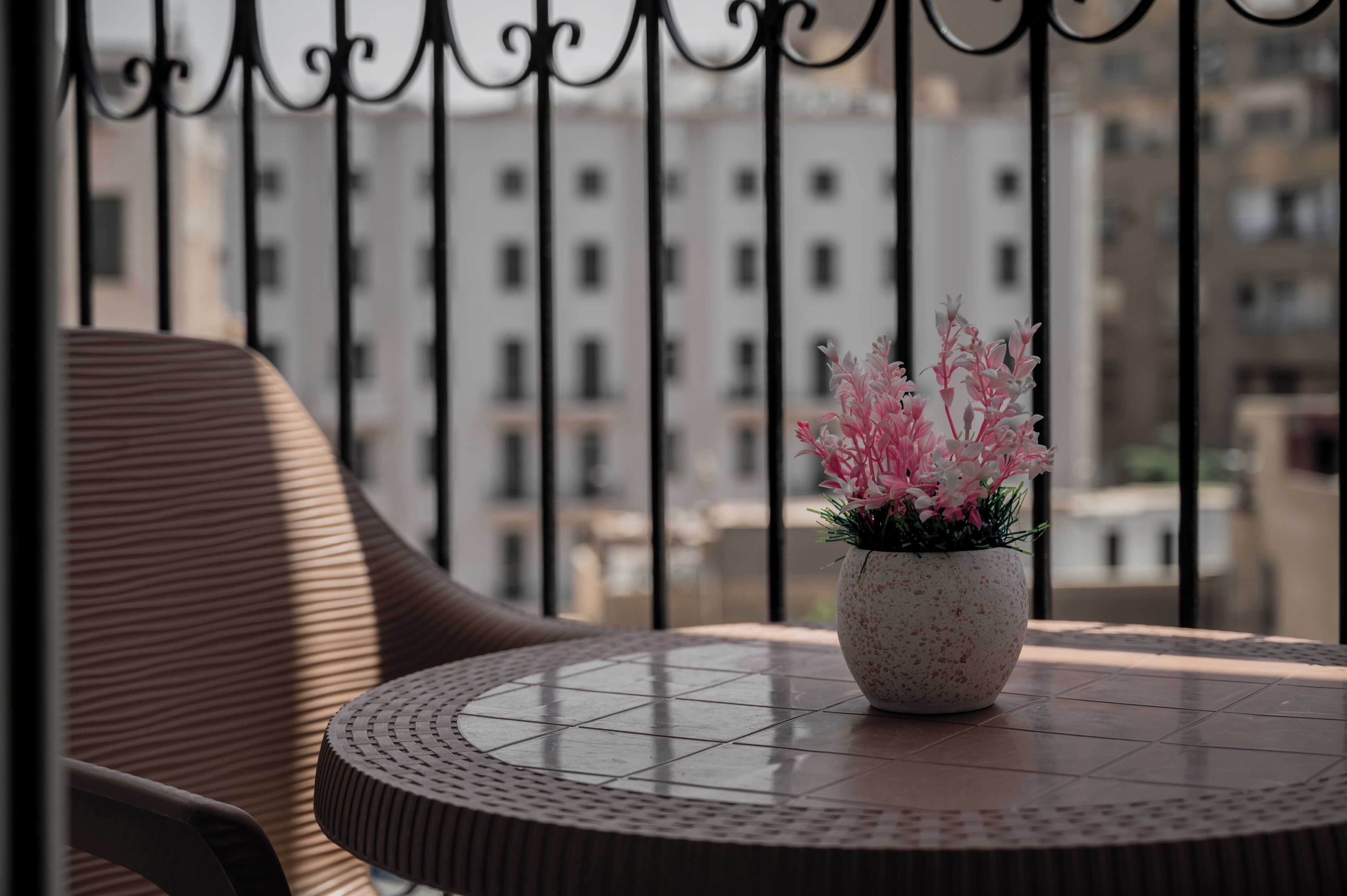 Una mesa redonda con una planta en maceta, una silla y vista de un edificio a través de una barandilla de metal.