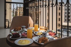 A balcony with a breakfast spread including croissants, eggs, and juice, overlooking a cityscape. - Royal Hotel (Cairo)