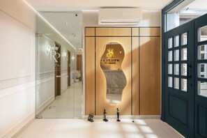 Zona de recepción de hotel con pared de vidrio, mostrador de madera y puerta azul oscuro.