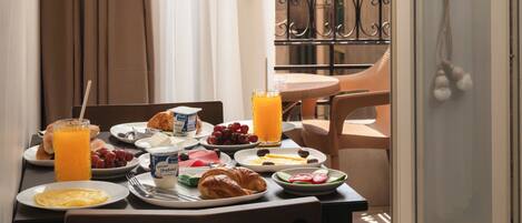 A breakfast table with plates of food, a glass of orange juice, and a window with curtains.