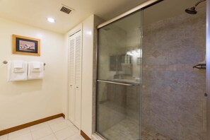 Kylpyhuoneessa on lasiseinäinen suihkukaappi, pyyhekoukku pyyhkeineen ja seinällä oleva kehystetty kuva.