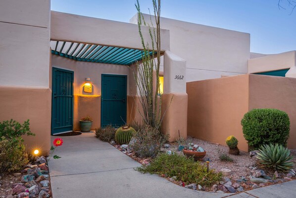 A building with a number '3662' on the wall, a blue door, and a garden with various plants and a cactus.