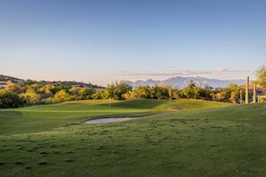 A golf course with a flag, a pond, and distant mountains.