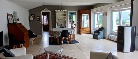 A spacious living area with a dining table and chairs, a sofa, and a large window providing natural light.