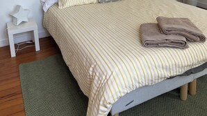Una cama bien hecha con ropa de cama a rayas, una lámpara de noche y una planta en maceta, junto con una luz nocturna con forma de estrella.