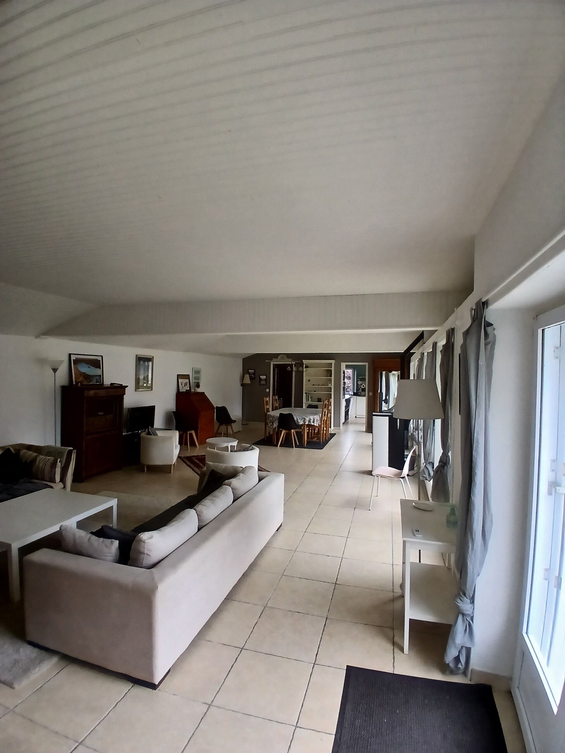 A spacious living room with a large sofa, a dining area, and a kitchen in the background.