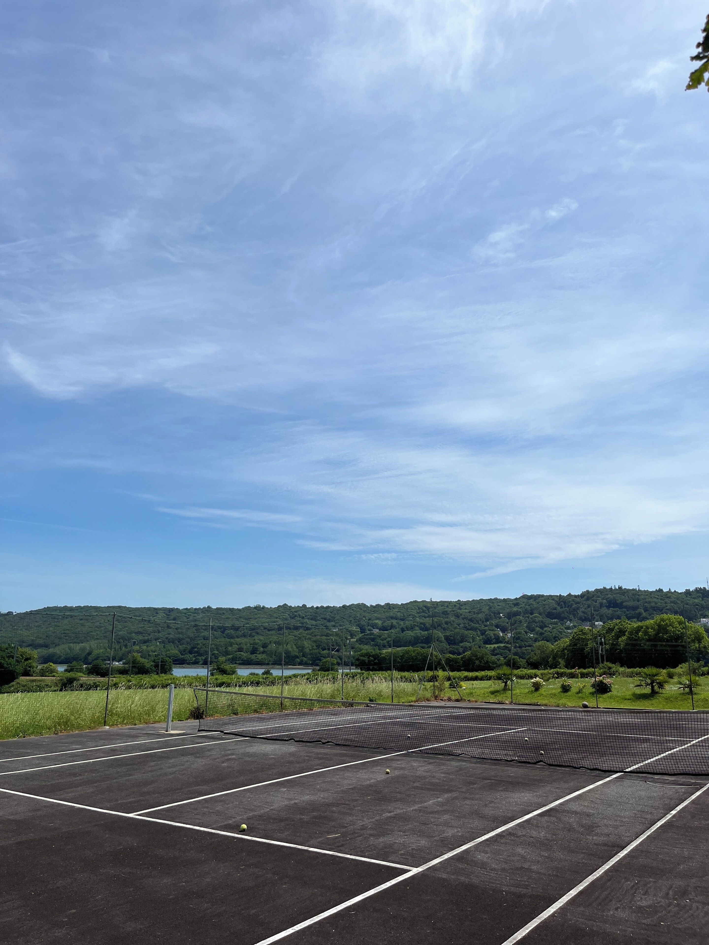 Un court de tennis avec un filet, entouré de verdure et avec un lac en arrière-plan.
