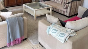Una sala de estar con un sofá, sillones, una mesa de centro, un televisor y un aparador.