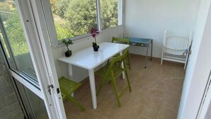 A small room with a table and chairs, a window with a view of greenery, and a white cabinet. - Villa- Nea Kalikrateia - 2-bdroom Apartment (Nea Propontida)