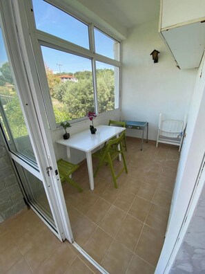A small room with a table and chairs, a window with a view of greenery, and a white cabinet. - Villa- Nea Kalikrateia - 2-bdroom Apartment (Nea Propontida)