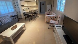 A living room with a sofa, a coffee table, a TV, and a dining area with chairs and a table. - Villa- Nea Kalikrateia - 2-bdroom Apartment (Nea Propontida)