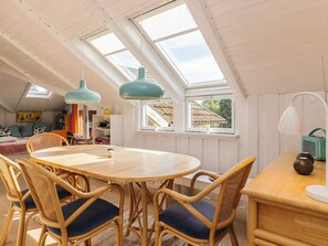 A dining area with a round wooden table and wicker chairs, a ceiling fan, and a view through a skylight.