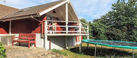 Un edificio rojo con balcón, un trampolín y una banca.