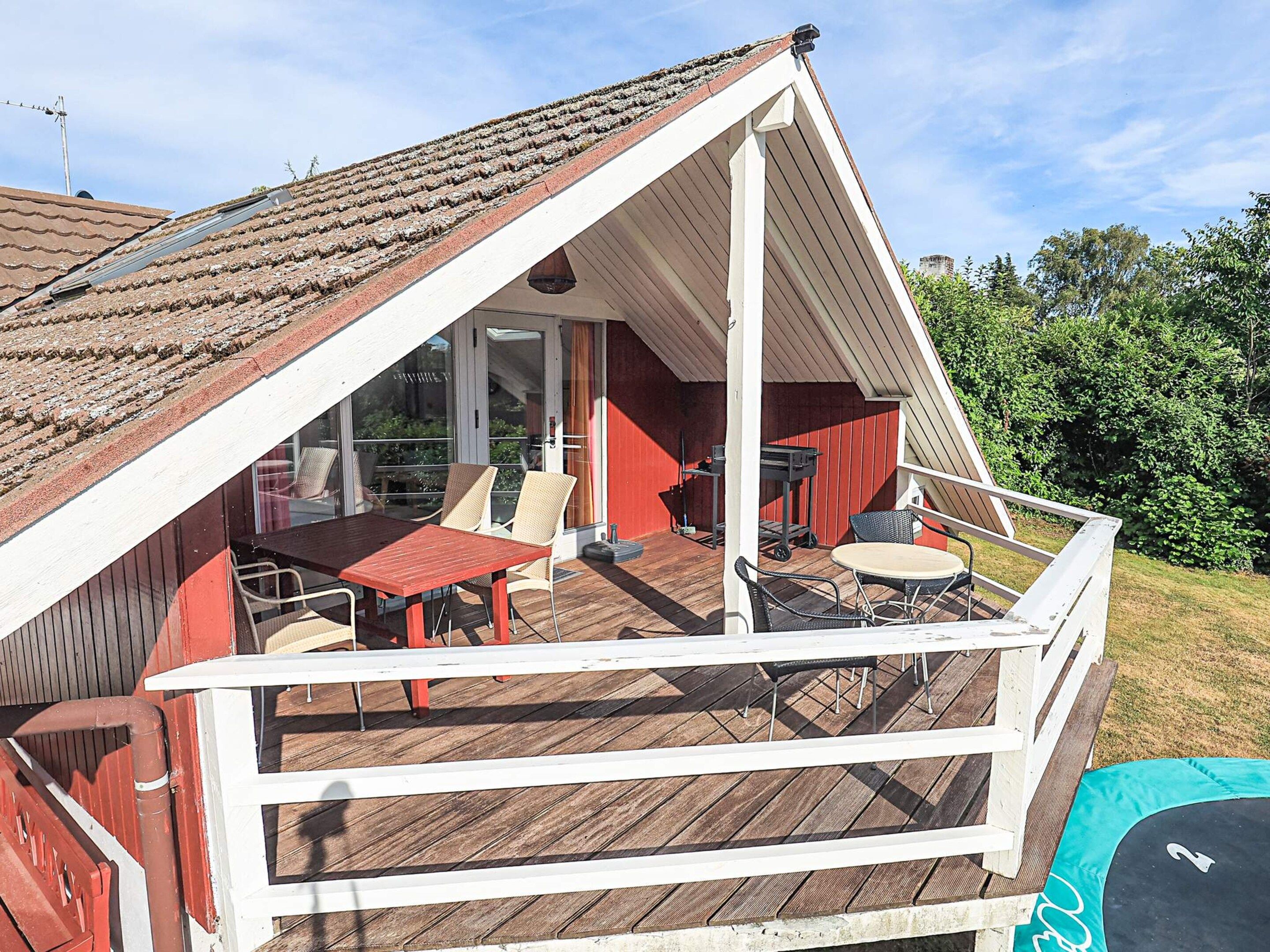 Ein überdachter Außenbereich mit Holzterrasse, Tisch mit Stühlen und Grill.