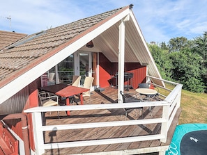 Un espacio al aire libre techado con piso de madera, una mesa con sillas y una parrilla.