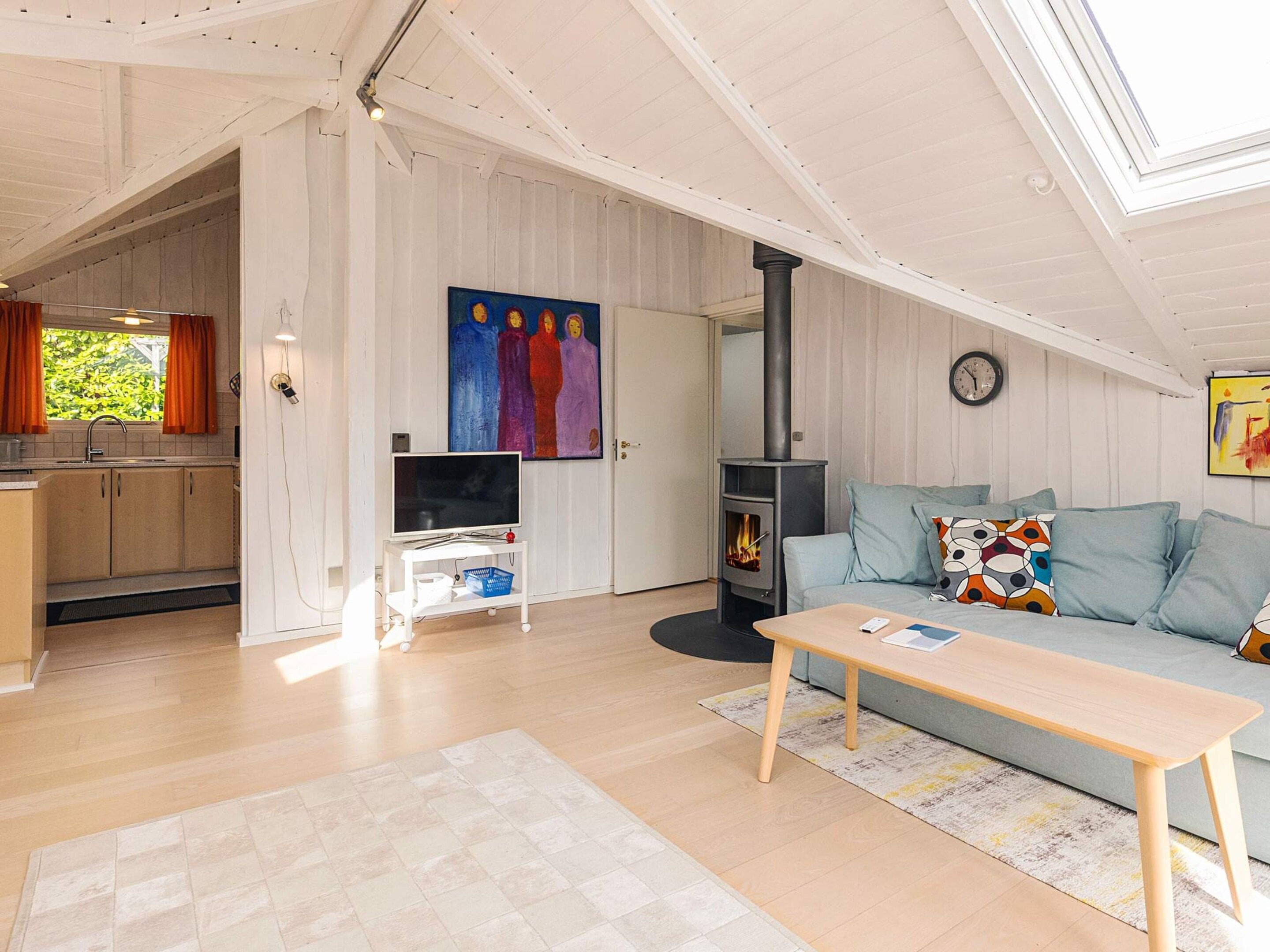 A cozy living room with a sofa, a television, a fireplace, and a kitchen area visible through an open door.