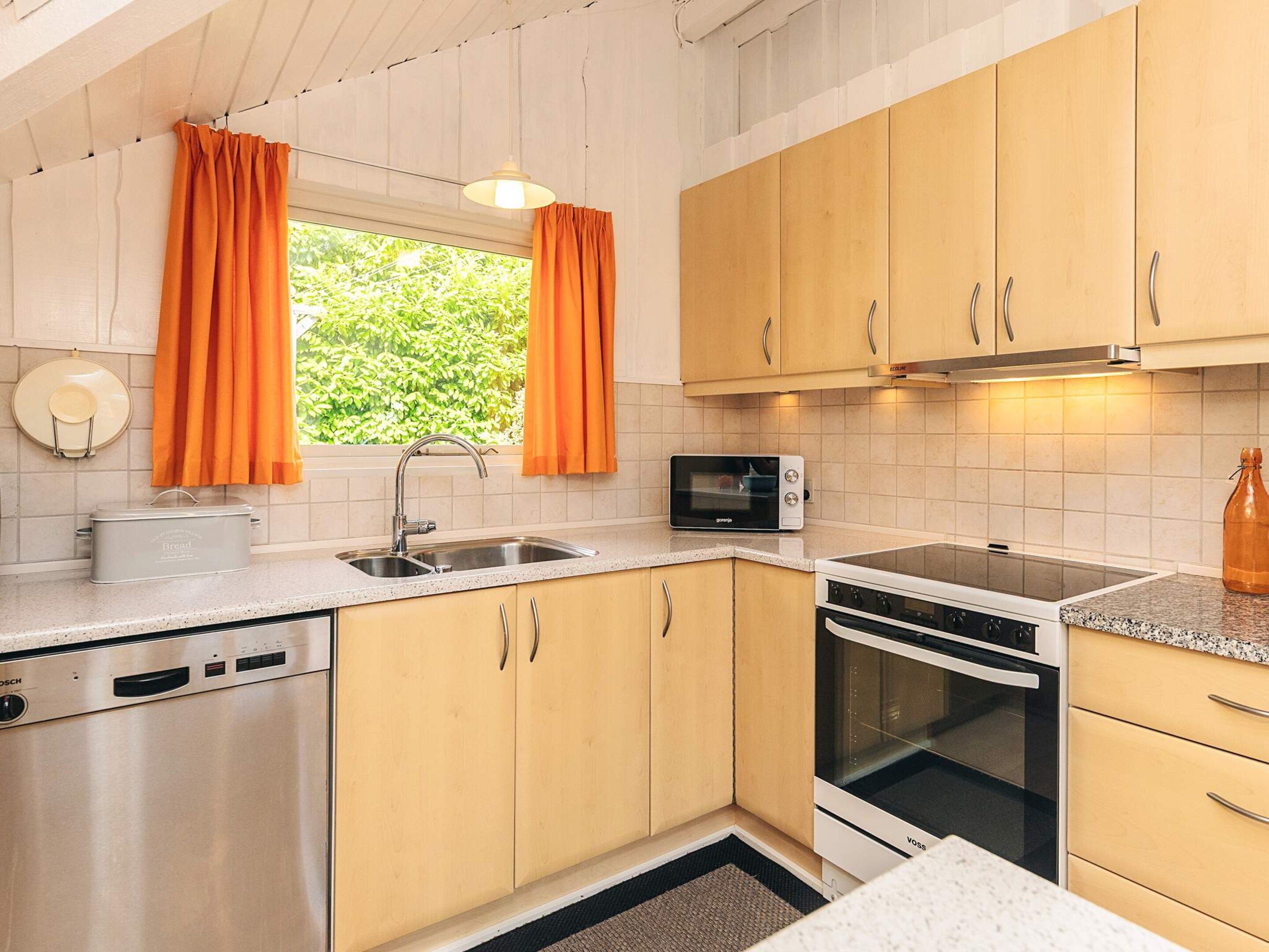 A compact kitchen with a dishwasher, microwave, stove, and a window with curtains.
