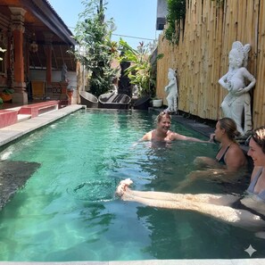 Una piscina con cerramiento de madera, estatuas de piedra y una zona cubierta con columnas.