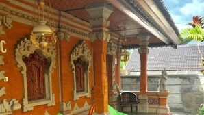 Un espacio de estar al aire libre techado, con cojines, suelo de baldosas y una pared decorativa.