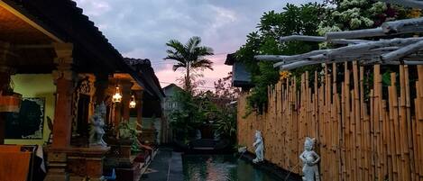 A courtyard with a pool, statues, and a bamboo fence.