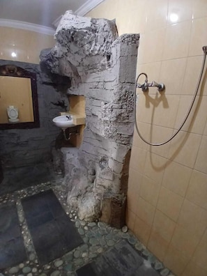 A bathroom with a stone wall, a sink, and a shower.