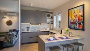 Une cuisine moderne avec des meubles gris, un îlot central doté de tabourets, un tableau accroché au mur et une vue par la fenêtre.