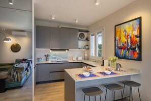 Eine moderne Küche mit grauen Schränken, einer zentralen Kochinsel mit Sitzgelegenheiten, einem Bild an der Wand und Blick durch das Fenster.