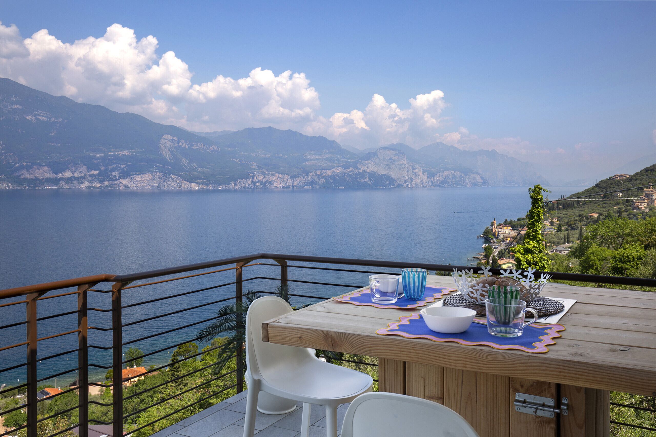 A wooden table with chairs, a view of a lake, mountains, and a distant village.