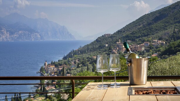 Une table avec deux verres à vin et une bouteille, donnant sur une ville côtière avec des montagnes en arrière-plan.