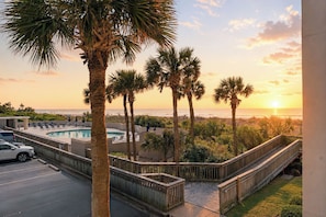 A pool area with palm trees, a wooden deck, and a view of the ocean at sunset. - South Hampton 107 Oceanview w/Pool & Beach (Myrtle Beach)