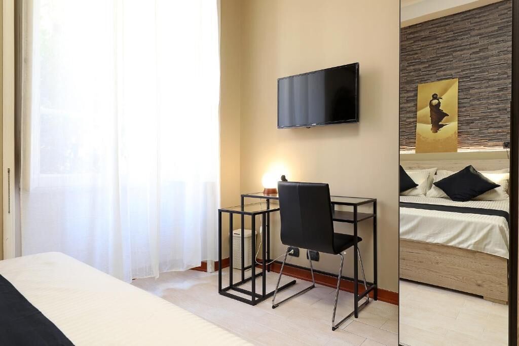 Una camera d'albergo con un letto, una scrivania con una sedia, una TV a muro e un quadro appeso.