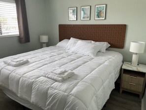 Ein ordentlich bezogenes Bett mit weißer Bettwäsche, einem Kopfteil und einem Nachttisch mit einer Lampe.