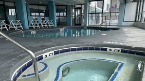 An indoor swimming pool with a tiled edge, a shallow water sign, and lounge chairs.