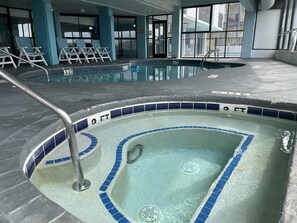 An indoor swimming pool with a tiled edge, a shallow water sign, and lounge chairs.