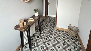 A hallway with patterned floor tiles, a wooden bench with decorative items, a wall-mounted light fixture, and a door leading to another room. - Les figuiers Charming stone house Pets welcome (Gonneville-Le Theil)