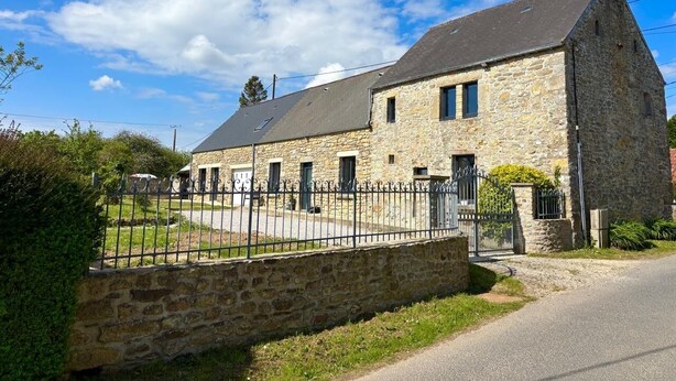 A stone building with a metal fence, a paved driveway, and a clear sky. - Les figuiers Charming stone house Pets welcome (Gonneville-Le Theil)
