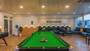 A pool table with cue sticks and balls, a sofa, and a wall with a hashtag sign.